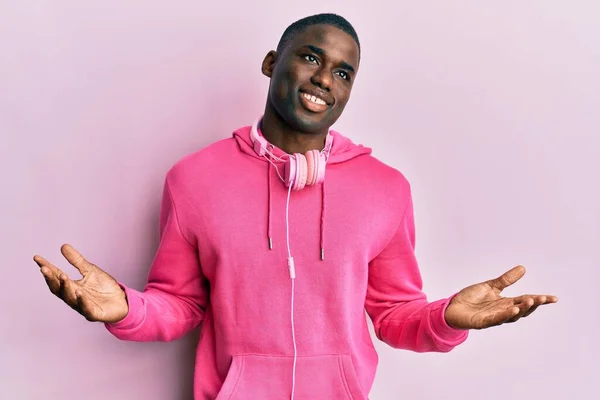 年轻的非洲裔美国人穿着运动服 用耳机毫无头绪地 困惑地微笑着举起胳膊和双手 怀疑概念 — 图库照片