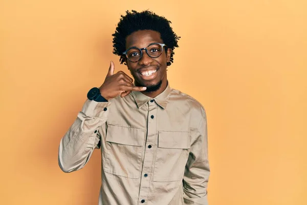 若いアフリカ系アメリカ人の男性がカジュアルな服を着て 眼鏡を手や指で電話で話すような携帯電話のジェスチャーをして笑顔 コミュニケーションの概念 — ストック写真