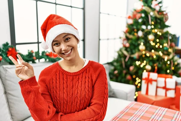 Kısa saçlı, ispanyol bir kadın kanepeye oturmuş gülümsüyor ve parmaklarını zafer işareti yaparken gösteren kameraya bakıyor. İki numara.. 