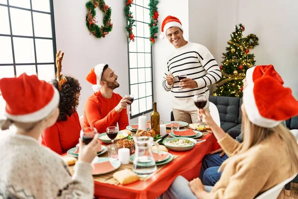 Mutlu bir şekilde gülümseyen bir grup genç Noel yemeği yiyor ve evde kadeh kaldırıyor..