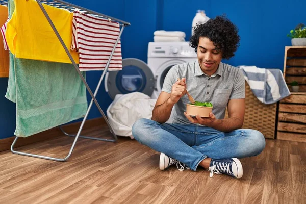 Young Hispanic Man Eating Salad Waiting Washing Machine Laundry Room — стоковое фото