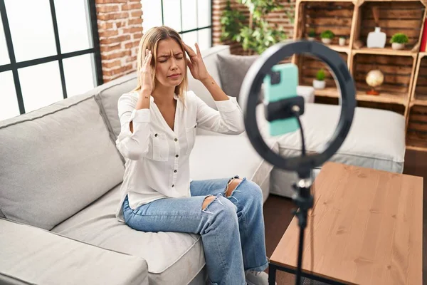 Sarışın genç bir kadın evde akıllı telefonuyla video kaydı yapıyor. Başı ağrıyor çünkü stres altında. migren ağrısı. 