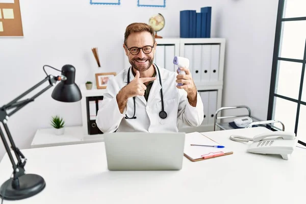 Médico Mediana Edad Sosteniendo Termómetro Clínica Sonriendo Feliz Señalando Con — Foto de Stock