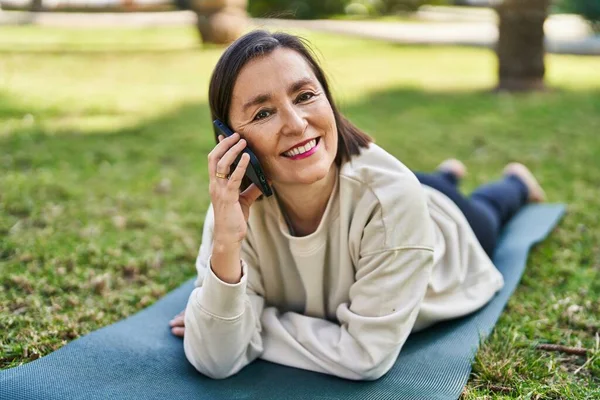 中世の女性は公園でハーブに横たわっているスマートフォンで話しています — ストック写真