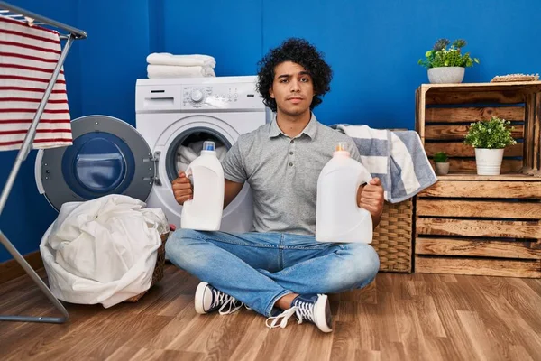 Hispanic Man Curly Hair Doing Laundry Holding Detergent Bottles Skeptic — стоковое фото