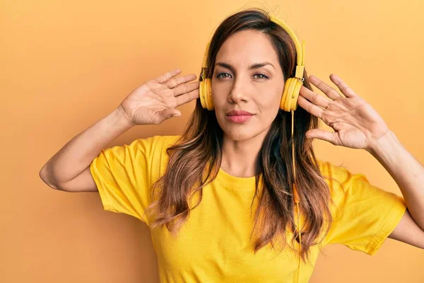 Young latin woman listening to music using headphones relaxed with serious expression on face. simple and natural looking at the camera.