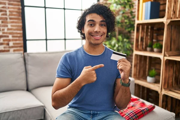 Hispanic Man Curly Hair Holding Credit Card Smiling Happy Pointing — Stock fotografie