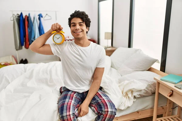 Ung Latinamerikansk Man Håller Väckarklocka Sitter Sovrummet Ser Positiv Och — Stockfoto
