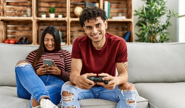 Video oyunu oynayan adam ve evde akıllı telefon kullanan kadın..