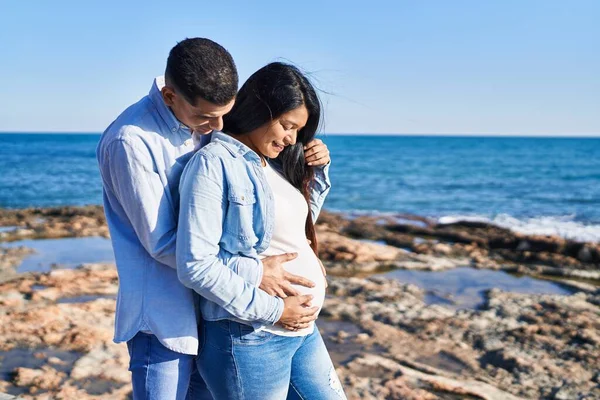 Genç Latin çift deniz kenarında karnına bebek dokunuşu bekliyor.