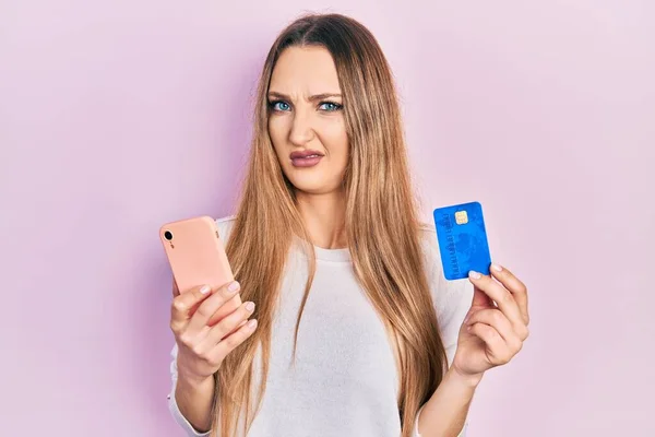 Młoda Blondynka Trzymająca Smartfona Kartę Kredytową Bez Pojęcia Zdezorientowana Ekspresja — Zdjęcie stockowe