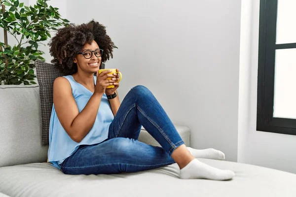 Genç Afro-Amerikan kadın gülümseyerek evde kahve içiyor.
