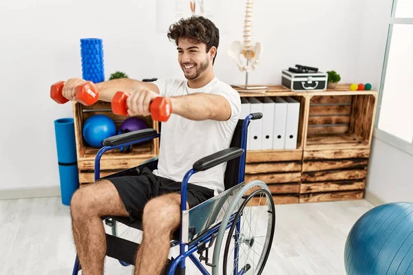 Young Hispanic Man Sitting Wheelchair Doing Rehab Using Dumbbells Clinic — Stockfoto