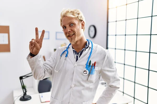 Jonge Blonde Man Doktersuniform Stethoscoop Kliniek Glimlachend Naar Camera Kijkend — Stockfoto