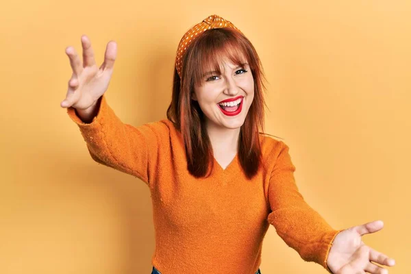 红头发的年轻女人穿着休闲的橙色毛衣 微笑着看着相机 张开双臂拥抱 欢快的表达拥抱幸福 — 图库照片