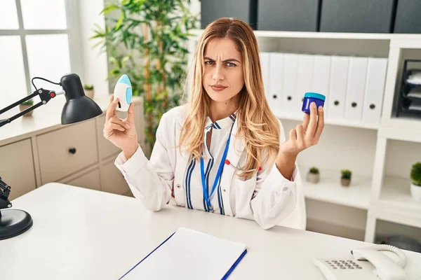 Young Blonde Doctor Woman Holding Medicine Products Breath Better Skeptic — Zdjęcie stockowe