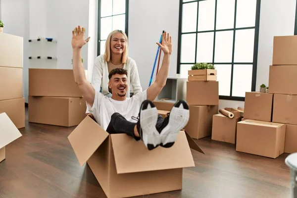 Young caucasian couple smiling happy playing with cardboard box as a car at new home.