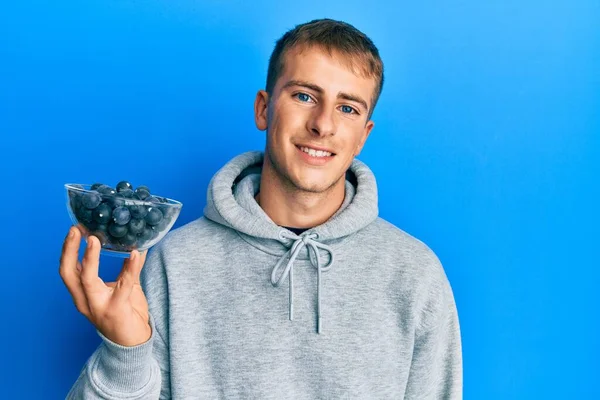 Young Caucasian Man Holding Bowl Blueberries Looking Positive Happy Standing — стоковое фото