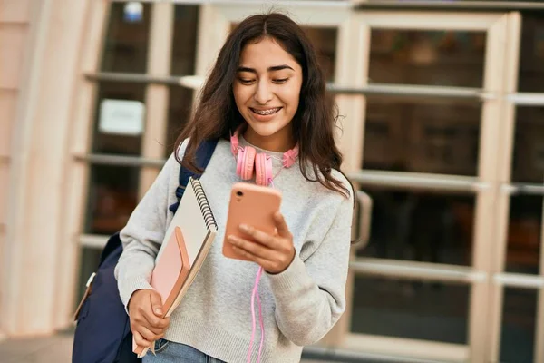Genç ortadoğulu kız şehirde akıllı telefon kullanarak mutlu bir şekilde gülümsüyor..