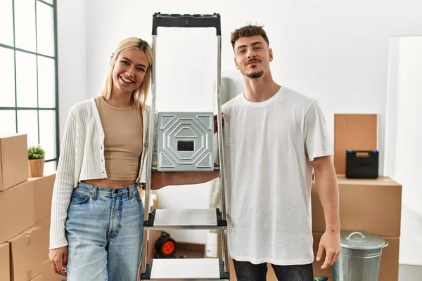 Yeni evimizde işçi merdivenleri tutarken mutlu gülümseyen beyaz bir çift..