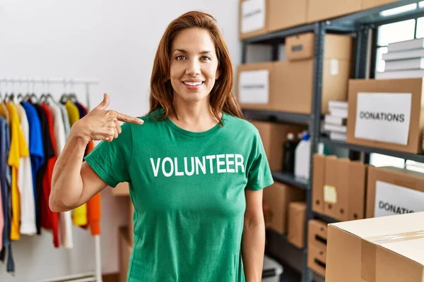 Bağışlarda gönüllü tişört giyen orta yaşlı İspanyol kadın mutlu ve gururlu bir kendini işaret ediyor. 