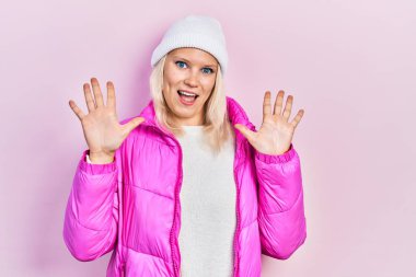 Güzel, beyaz, sarışın, yün şapkalı, kışlık paltolu bir kadın on numaralı parmaklarıyla onu gösterirken kendine güvenen ve mutlu bir şekilde gülümsüyor.. 