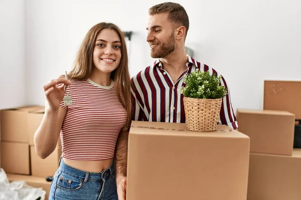 Genç beyaz çift mutlu bir şekilde gülümsüyor. Karton kutu ve yeni evin anahtarını tutuyorlar..