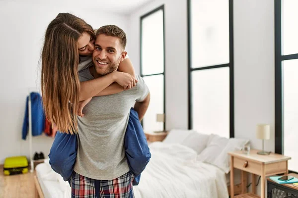 Genç beyaz bir adam yatak odasında kadını sırtında tutuyor..