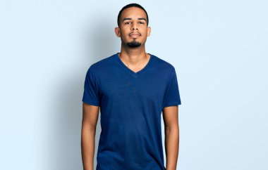 Gündelik tişört giyen Afro-Amerikan genç adam yüzünde ciddi bir ifadeyle rahatlamış. Basit ve doğal bir şekilde kameraya bakıyorsun.. 