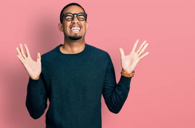 Sıradan kıyafetler ve gözlük takmış genç Afro-Amerikalı adam başarı için çılgın ve çılgın kutlamalar yapıyor kollarını kaldırmış, gözlerini kapatmış heyecanlı çığlıklar atıyor. Kazanan konsept 