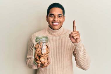 Genç, yakışıklı İspanyol adam elinde çikolata parçacıklı kurabiye kavanozuyla gülümseyen bir fikir ya da soru işareti yapan mutlu yüzlü, bir numara. 