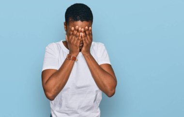 Genç Afro-Amerikalı kadın, günlük beyaz tişört giyiyordu. Üzücü bir ifade takınıyordu. Ağlarken yüzünü ellerle kapatıyordu. depresyon kavramı. 