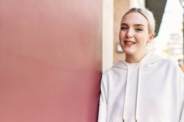 Modern beyaz saç stili ile genç ve güzel bir kadın mutlu bir şekilde dışarıda duvara yaslanıyor.