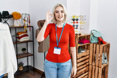 Perakende satış mağazasında yönetici olarak çalışan beyaz bir kadın gülümsüyor ve el ve parmaklarıyla tamam işareti yapıyor. başarılı ifade. 