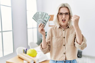İnşaat ofisindeki genç, beyaz bir kadın elinde parayla sinirlenmiş ve sinirlenmiş bir şekilde bağırıyor. Öfkeyle bağırıyor ve el kaldırıyor. 