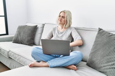 Genç, beyaz bir kadın evinde dizüstü bilgisayar kullanıyor. Elleri karnında kanepede oturuyor. Çünkü mide bulantısı ve acı verici bir hastalık var. Ağrı kavramı. 