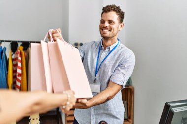 Genç İspanyol esnaf gülümseyerek giyim mağazasındaki müşterilere alışveriş torbaları veriyor..