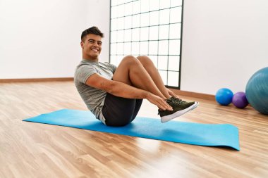 Genç İspanyol adam gülümsüyor spor merkezinde kendine güvenen karın kasları egzersizi yapıyor.
