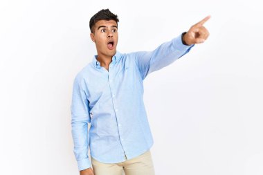 İş gömleği giyen genç İspanyol bir adam izole edilmiş arka planda dikiliyor. Parmakları önde, ağzı açık, şaşırmış, ön tarafta bir şey var. 