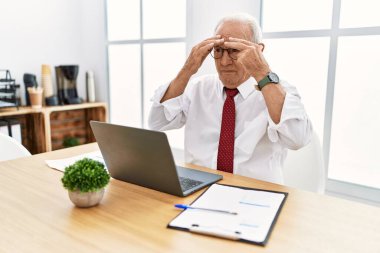 Ofiste çalışan kıdemli bir adam bilgisayarı kullanıyor. Yorgunluk ve baş ağrısı için gözlerini ovuşturuyor. Uykulu ve yorgun ifadeler kullanıyor. görme sorunu 