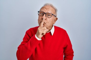 Gri saçlı yaşlı adam izole edilmiş arka planda duruyor ve dudakları parmaklarıyla sessiz olmak istiyor. sessizlik ve gizli konsept. 