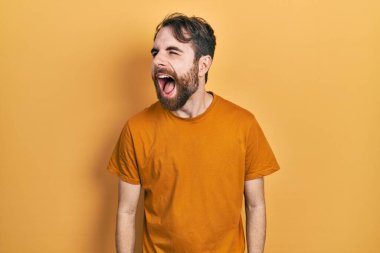 Sakallı, sıradan sarı tişörtlü, sinirli ve öfkeli sinirli sinirli, öfkeyle bağıran beyaz bir adam. öfke ve agresif konsept. 