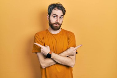 Sakallı, sarı tişörtlü, iki tarafı da parmaklarıyla gösteren beyaz bir adam. Farklı yönlerden. 