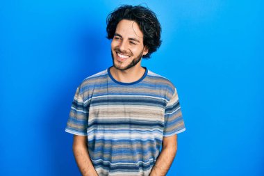 Handsome hispanic man wearing casual clothes over pink background looking away to side with smile on face, natural expression. laughing confident. 