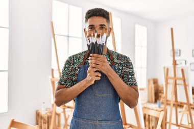 Genç Afrikalı Amerikalı sanatçı, resim stüdyosundaki fırçalarla ağzını kapayarak mutlu bir şekilde gülümsüyor..