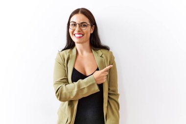 Genç esmer kadın izole edilmiş arka planda neşeli bir şekilde ayakta duruyor yüzünde gülümseme, mutlu ve doğal bir ifadeyle elleri ve parmaklarıyla kenarı işaret ediyor. 