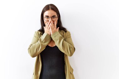 Genç esmer kadın izole edilmiş arka planda duruyor gülüyor ve utanıyor kıkırdıyor elleriyle ağzını kapatıyor, dedikodu yapıyor ve skandal konsepti yapıyor. 