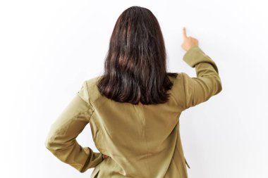 Young brunette woman standing over isolated background posing backwards pointing ahead with finger hand 