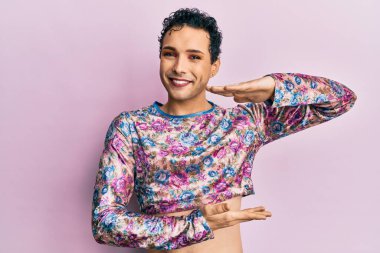 Makyaj yapan yakışıklı bir adam. Moda kıyafetleri giyiyor. Elleriyle işaret ediyor. Kameraya bakıp gülümsüyor. ölçüm kavramı. 