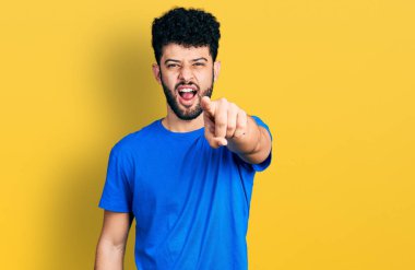 Mavi tişörtlü, sakallı genç Arap adam kameraya kızgın ve sinirli bir şekilde kızgın olduğunu gösteriyor. 